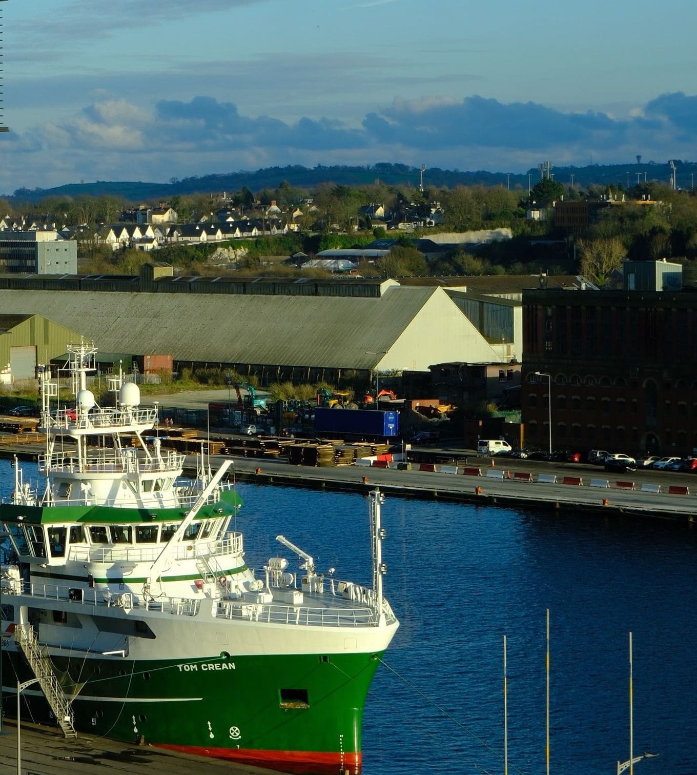 Un navire amarré à un quai de port, devant des entrepôts et des collines
